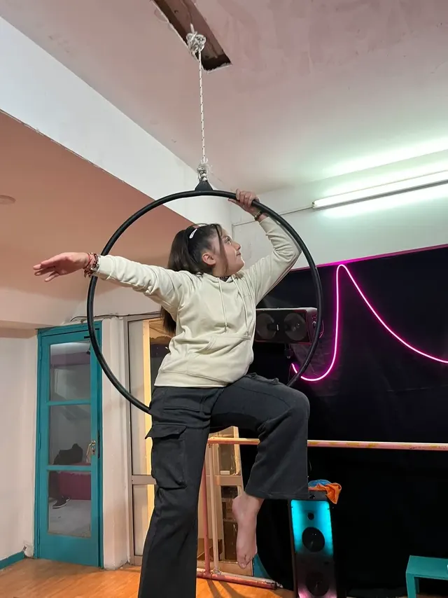 Alumna de pie en el aro del Estudio Melani Mitchell, con un pie apoyado en el aro y los brazos abiertos