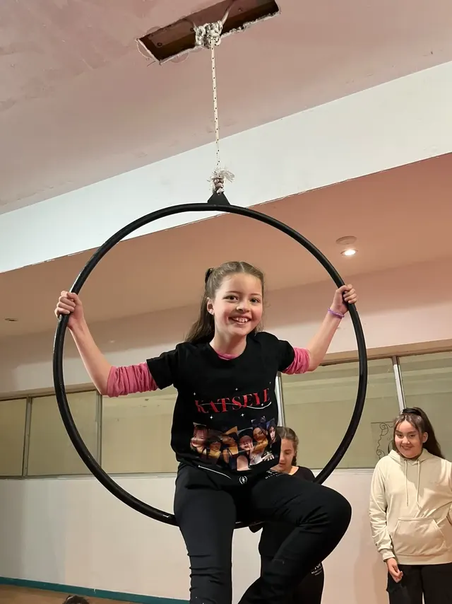 Alumna sentada en el aro del Estudio Melani Mitchell, sonriendo, con las dos manos tomadas del aro