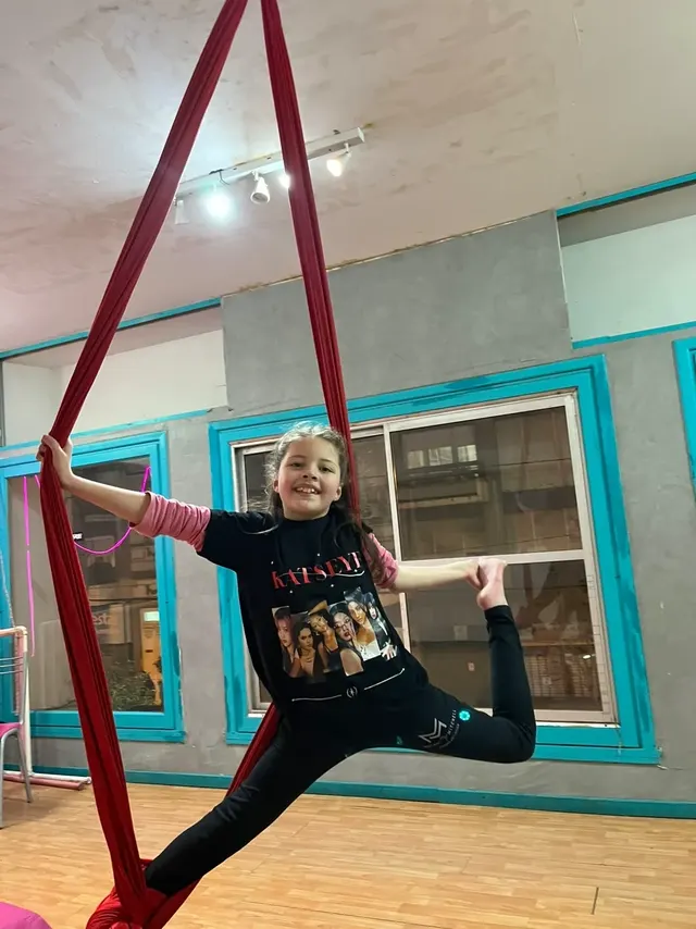 Alumna en split sobre la tela roja del Estudio Melani Mitchell, sostenida con una mano y la otra pierna estirada