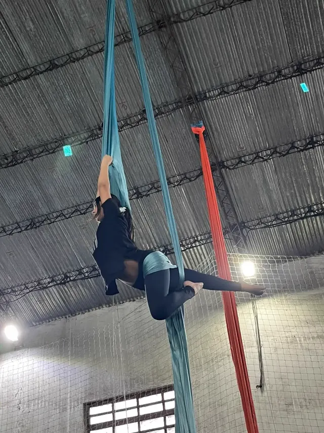 Alumna en figura sobre la tela turquesa del Gimnasio Alma, sostenida de la tela con una pierna estirada hacia el costado
